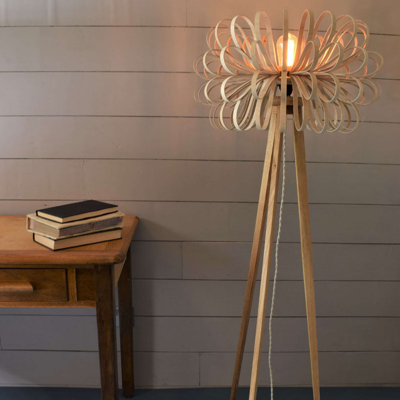 Modern wooden tripod floor lamp with loop design shade and exposed bulb next to vintage wooden table with books