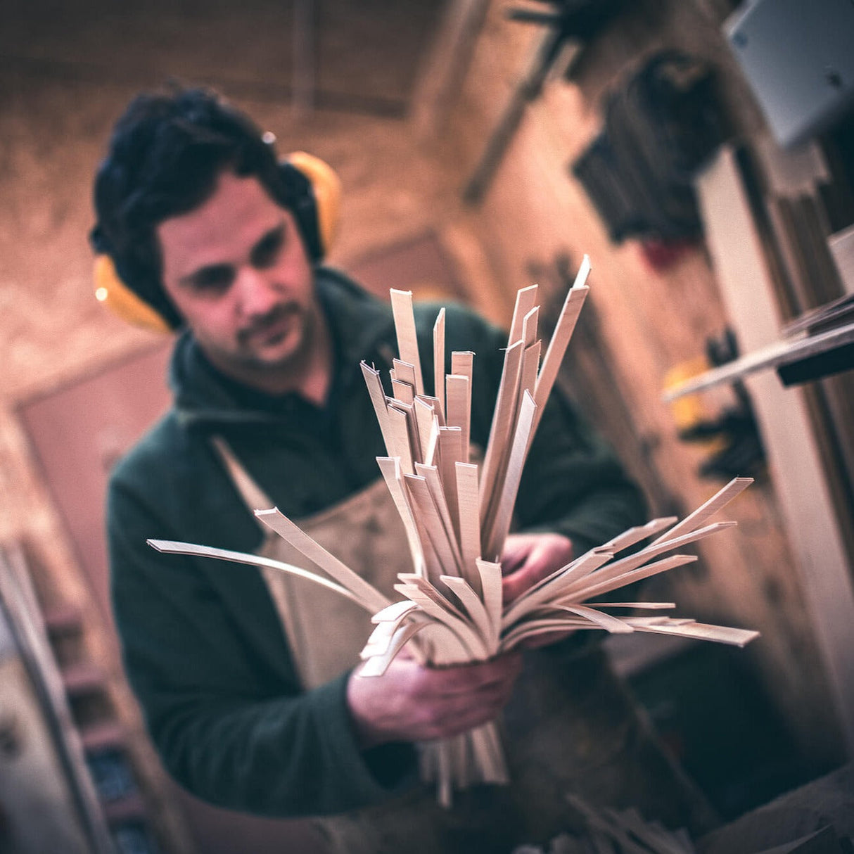 Craftsman in workshop wearing ear protection holding thin wooden strips for woodworking project