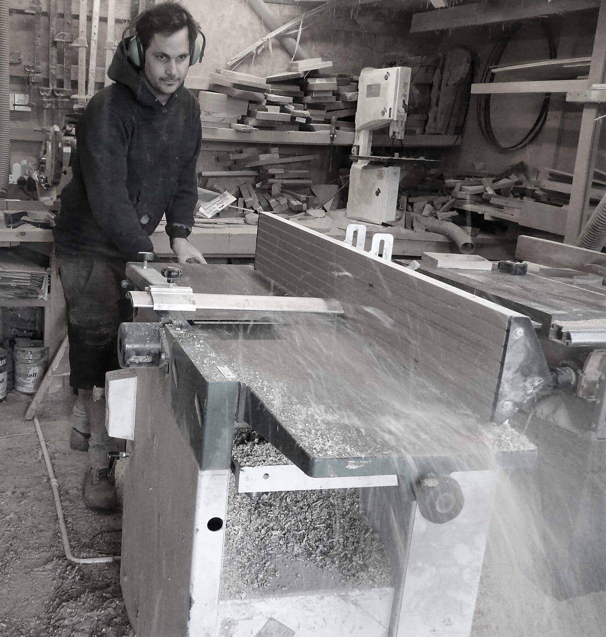 Carpenter using a table saw in a woodshop with wood planks and sawdust flying