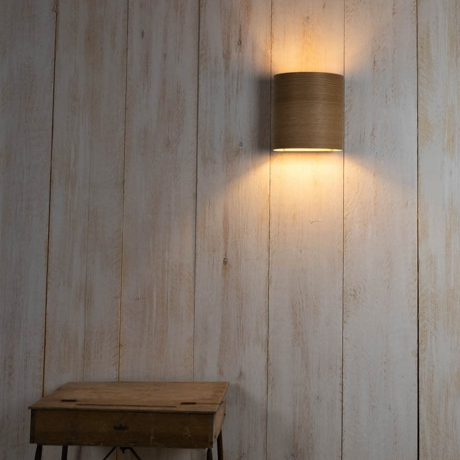 Modern cylindrical wooden wall light illuminating a rustic wooden wall above a small wooden table