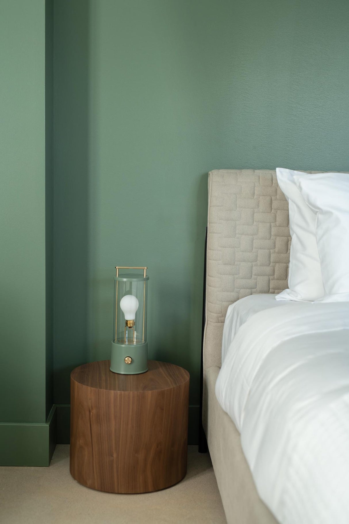 Modern Tala Muse portable lamp on wooden bedside table in green-walled bedroom with beige quilted bed
