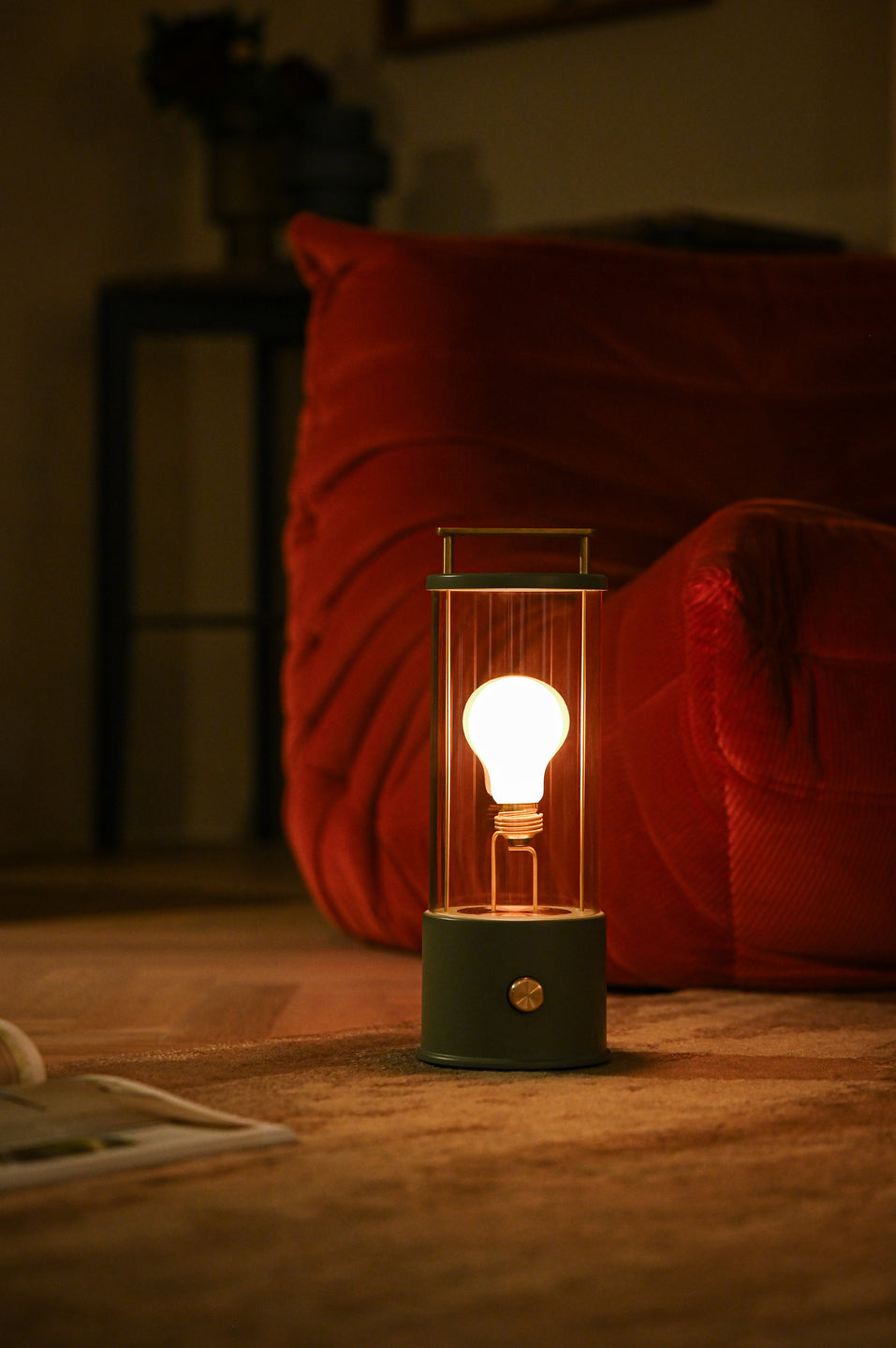 Tala Muse portable lamp glowing warmly on a rug beside a red velvet sofa in cozy living room