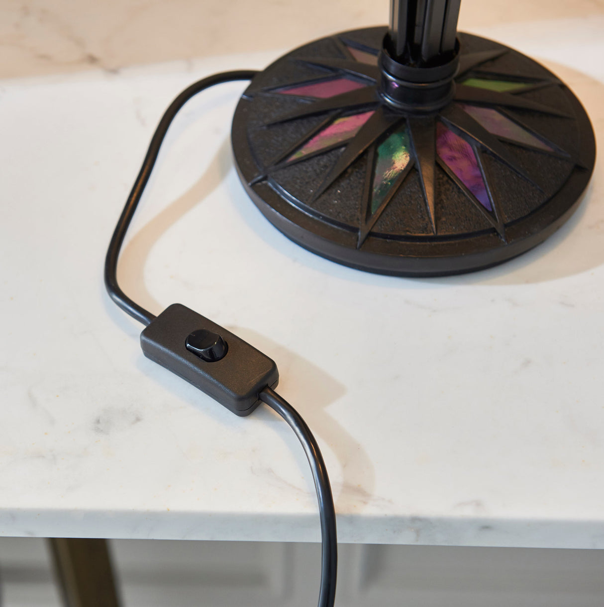 Close-up of black table lamp base with colorful star-shaped inlays and inline switch on white marble surface