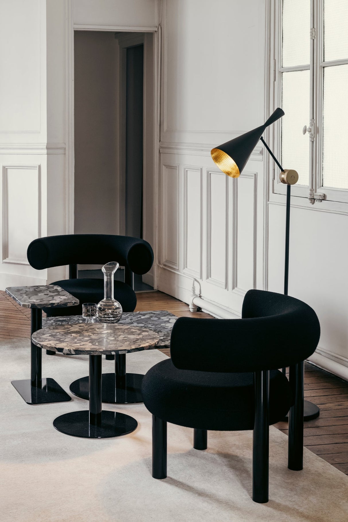 Modern black armchairs and marble side tables in stylish living room with black floor lamp and white paneled walls