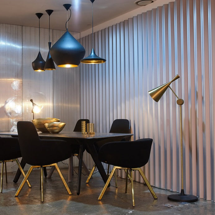 Modern dining room with black chairs, brass legs, brass floor lamp, and black pendant lights