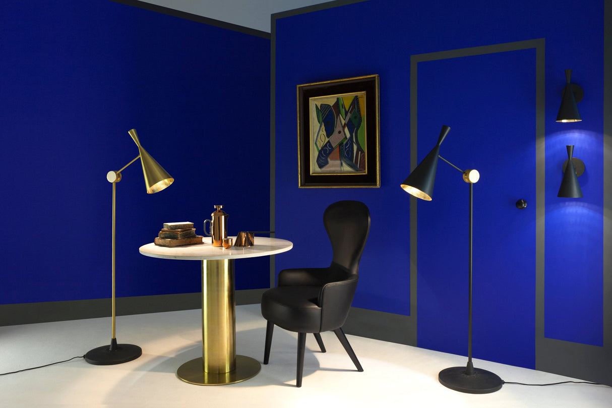 Modern living room with blue walls, brass floor lamps, black chair, marble and brass round table