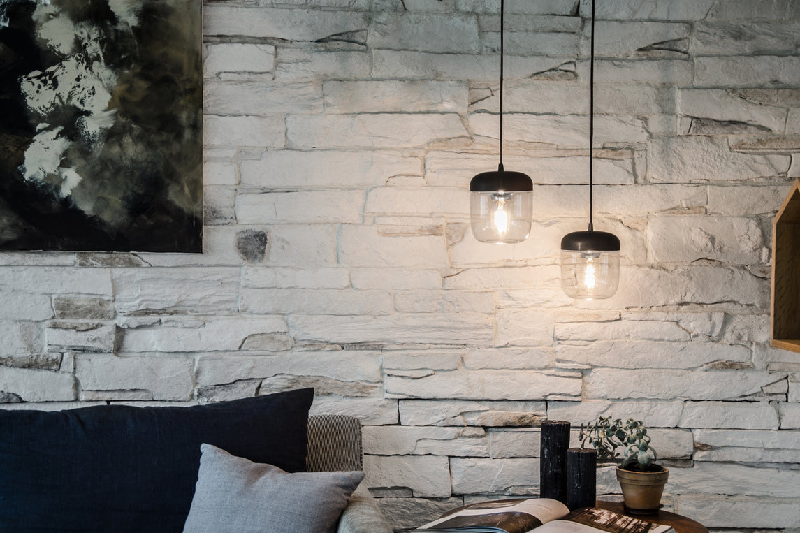 Modern living room with white stone wall, black pendant lights, dark cushions, and small plant on table
