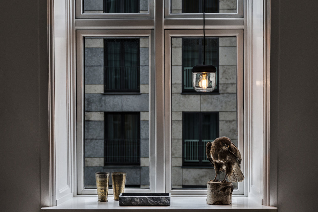 Modern black pendant light over windowsill with decorative hawk sculpture and gold cups in urban apartment