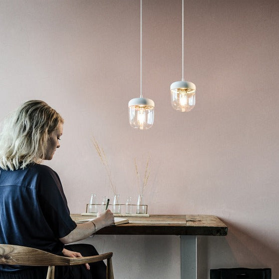 Woman writing at wooden table under modern white and brass pendant lights in minimalist room