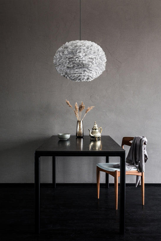 Modern dining room with black table, wooden chair, dried flowers in vase, brass teapot, and grey feather pendant lamp