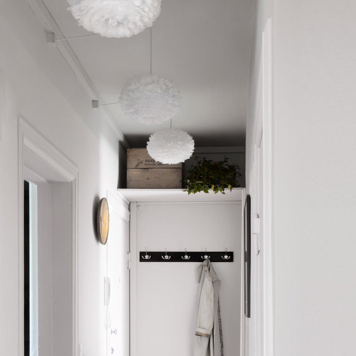 Modern white feather pendant lights in a minimalist hallway with coat rack and wooden crate shelf