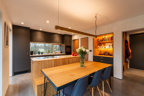 Modern kitchen and dining area with wood accents, black cabinets, concrete flooring, and pendant light