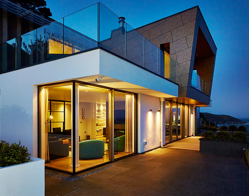 Modern illuminated cliff-side house with glass walls and ocean view at dusk