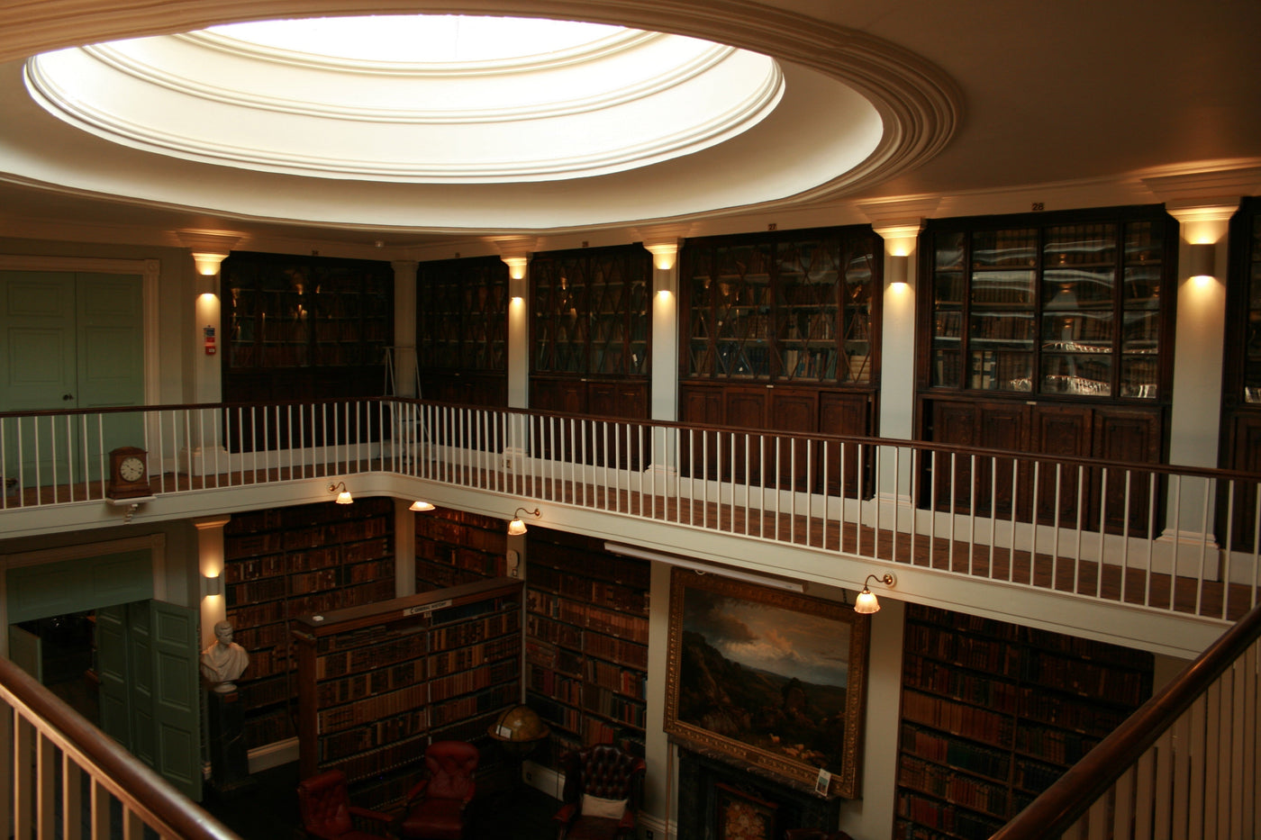 Interior of a historic library with wooden bookshelves, leather chairs, a bust statue, and a circular skylight
