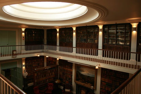 Interior of a historic library with wooden bookshelves, leather chairs, a bust statue, and a circular skylight