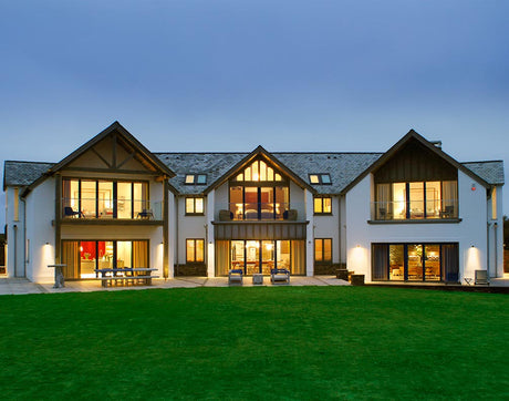 Modern large two-story house with illuminated windows, balconies, and green lawn at dusk