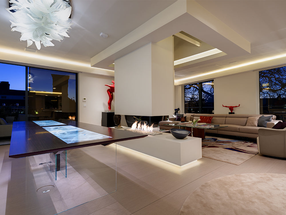 Modern living room with glass table, central fireplace, beige sectional sofa, and ambient LED lighting at dusk