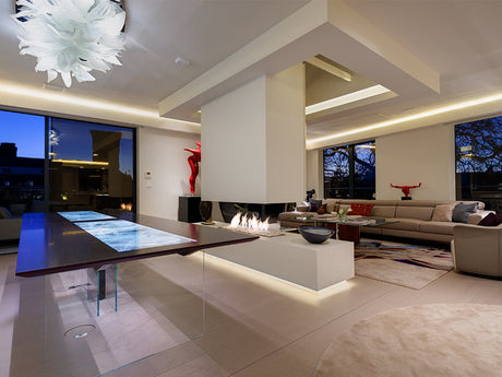 Modern living room with glass table, central fireplace, beige sectional sofa, and ambient LED lighting at dusk