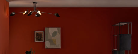 Modern living room with dark red wall, unique black chandelier, framed abstract and tree artwork, and black metal shelving unit