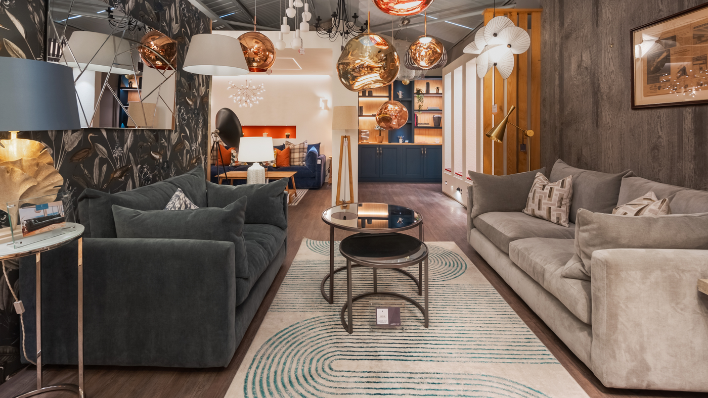 Modern living room with dark gray and beige sofas, patterned rug, gold accents, and hanging pendant lights