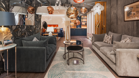 Modern living room with dark gray and beige sofas, patterned rug, gold accents, and hanging pendant lights