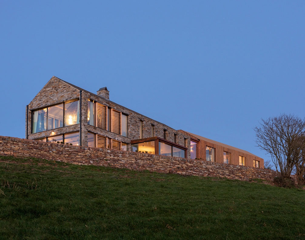 Modern stone and wood house on hill with large windows at dusk and clear blue sky