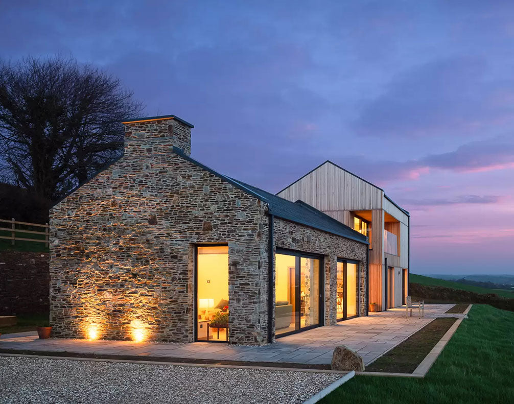 Modern stone and wood country house illuminated at dusk with large glass windows and landscape views