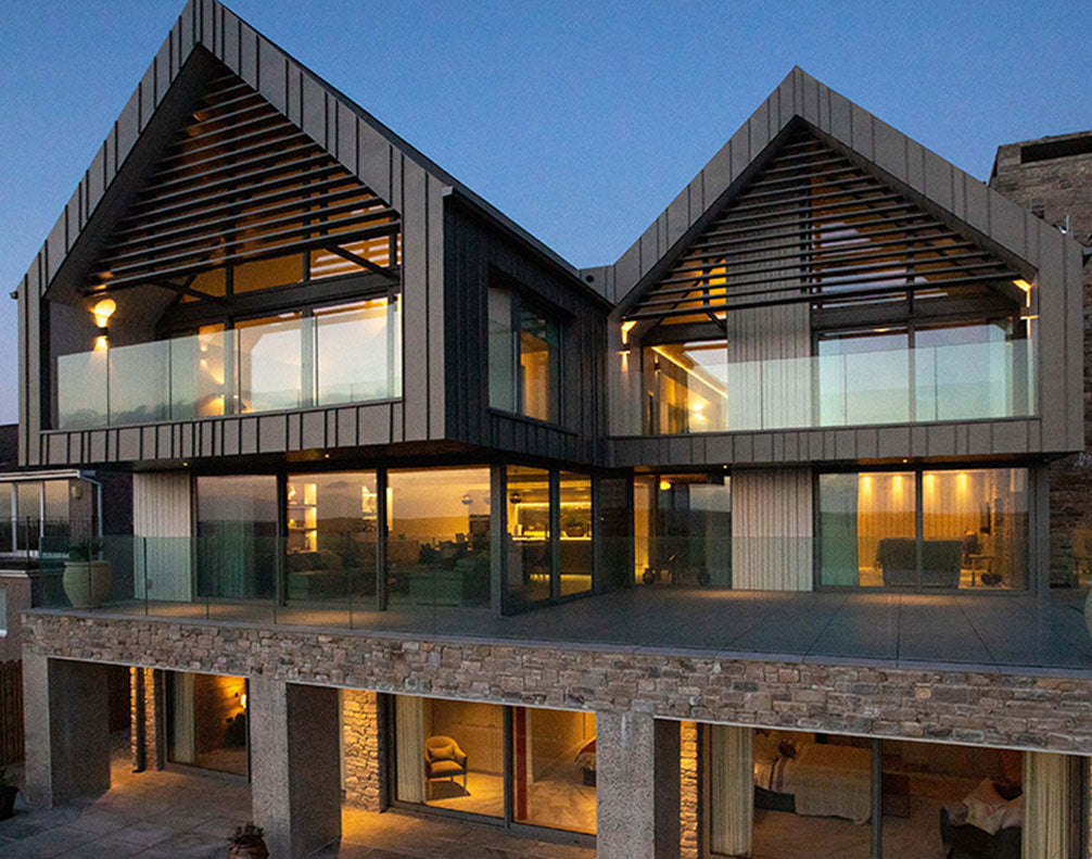 Modern three-story house with glass balconies, stone facade, and warm interior lighting at dusk