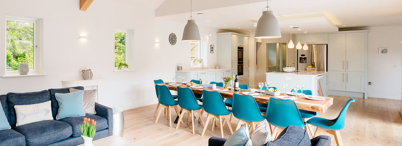 Bright modern open kitchen and dining area with wooden table, blue chairs, and cozy living room seating