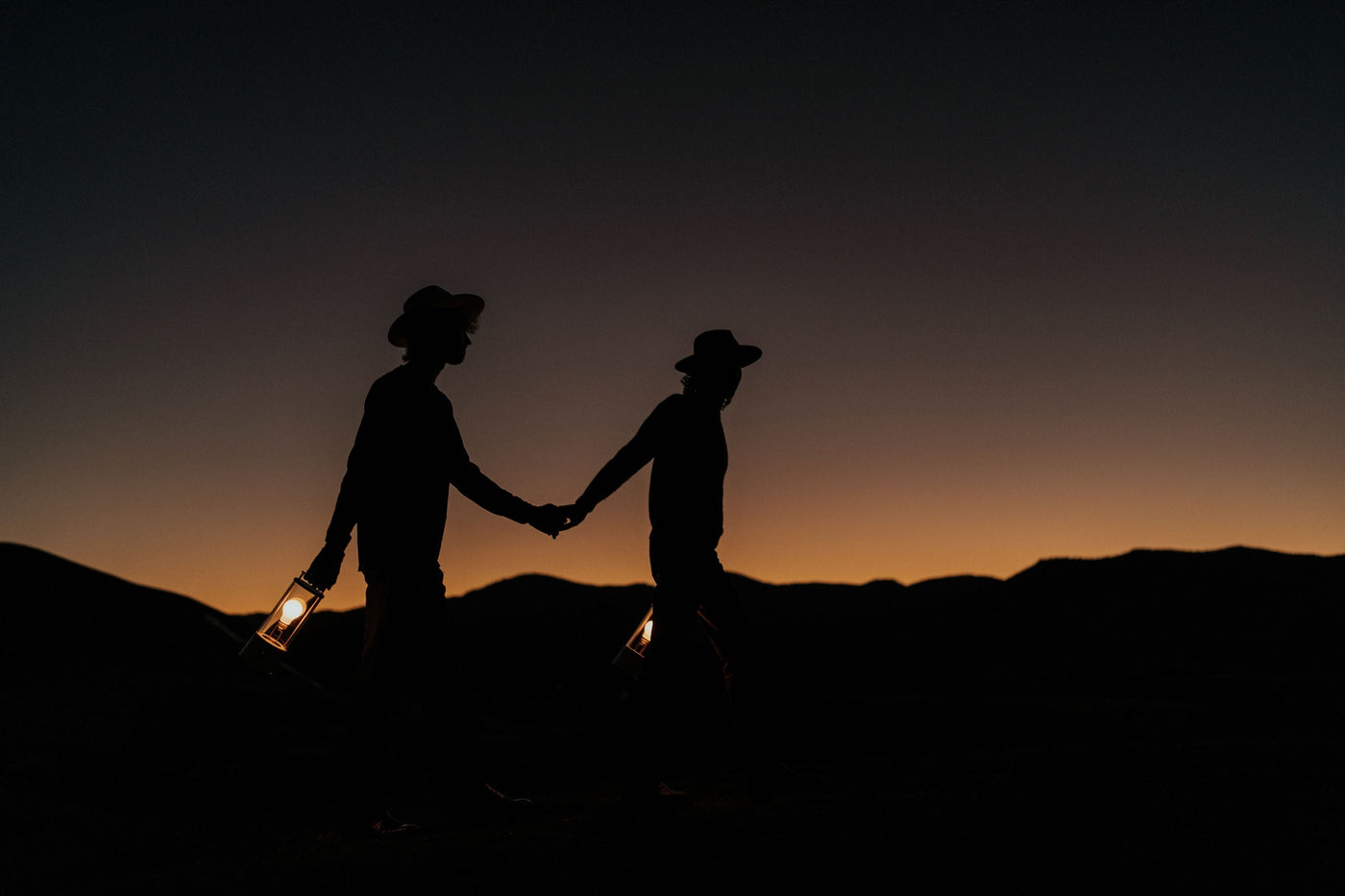 Silhouetted couple holding hands and lanterns walking at sunset with mountain backdrop