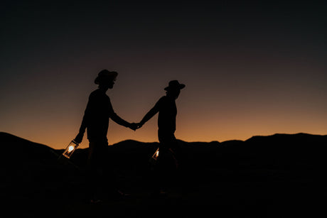 Silhouetted couple holding hands and lanterns walking at sunset with mountain backdrop