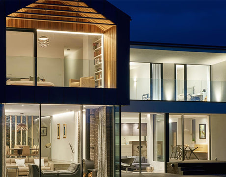 Modern two-story house with large glass windows, illuminated interior at night, showing living and dining areas