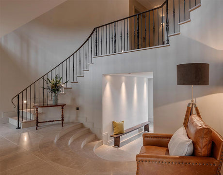 Elegant living room with curved staircase, leather armchair, wooden table with vase, and modern floor lamp