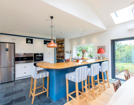 Modern kitchen with blue island, wood countertop, striped bar stools, stainless fridge, and large windows