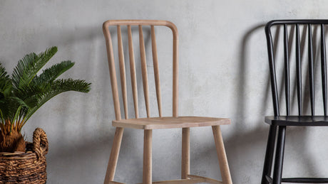 Light wood dining chair with vertical slats next to black chair and woven basket plant