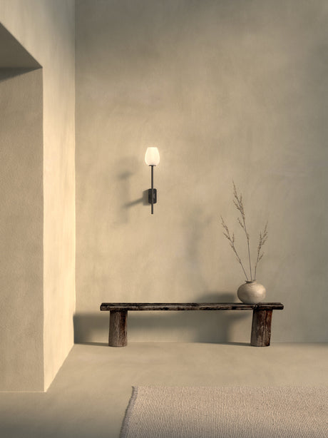 Minimalist interior with black wall sconce, wooden bench, and round vase with dried branches