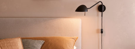 Modern black wall-mounted bedside lamp above beige upholstered headboard with decorative pillows