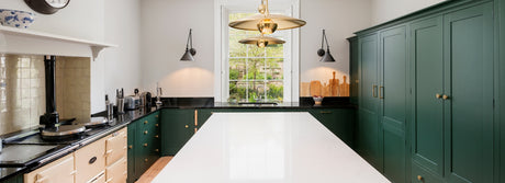 Modern kitchen with green cabinets, white island, black countertops, and gold pendant lights