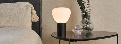 Modern touch lamp with frosted glass shade on black base on round metal side table with decorative glass vases