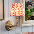 Wall sconce with a colorful lampshade next to a painting and floral arrangement on a light blue wall.