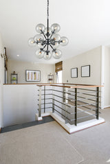 Modern stairwell with metal railing and wood handrails under a black multi-globe glass chandelier