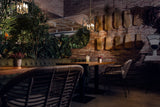 Cozy restaurant interior with wooden tables, wicker chairs, green plants, brick walls, decorative hanging boards, and a vintage scale