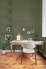 Cozy home office with wooden desk, patterned chair, green walls, potted plants, and desk lamp