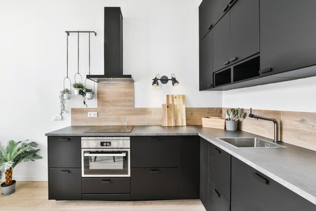 Modern kitchen with black cabinets, concrete countertop, wooden backsplash, and hanging plants