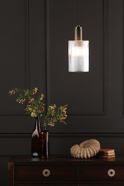 Dar Nikolas ribbed glass pendant light with solid brass fixture above dark wood dresser with vases and decorative object