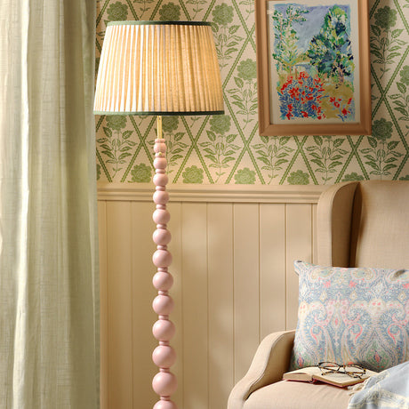 Pink floor lamp in a room with a floral painting and beige chair.
