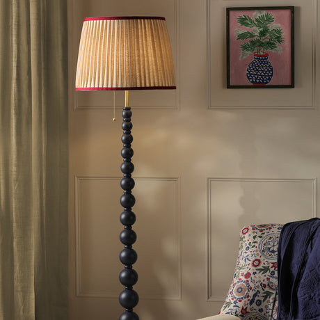 Decorative floor lamp with pleated shade in a room with a floral armchair and framed artwork.