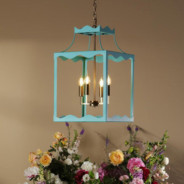 A turquoise blue hanging lantern-style chandelier with lit candle bulbs is suspended above a round table decorated with a large floral arrangement in pink, white, yellow, and burgundy flowers against a warm beige wall.