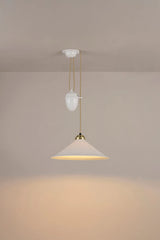 Original BTC Cobb Rise and Fall. Modern pendant light with a beige shade and gold fixture on a plain wall.