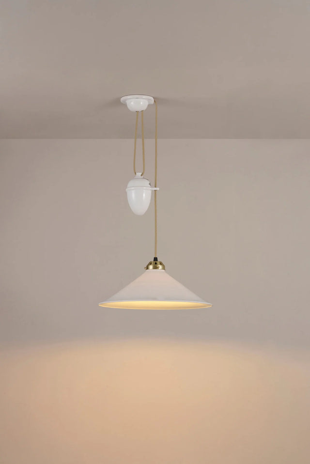 Original BTC Cobb Rise and Fall. Modern pendant light with a beige shade and gold fixture on a plain wall.
